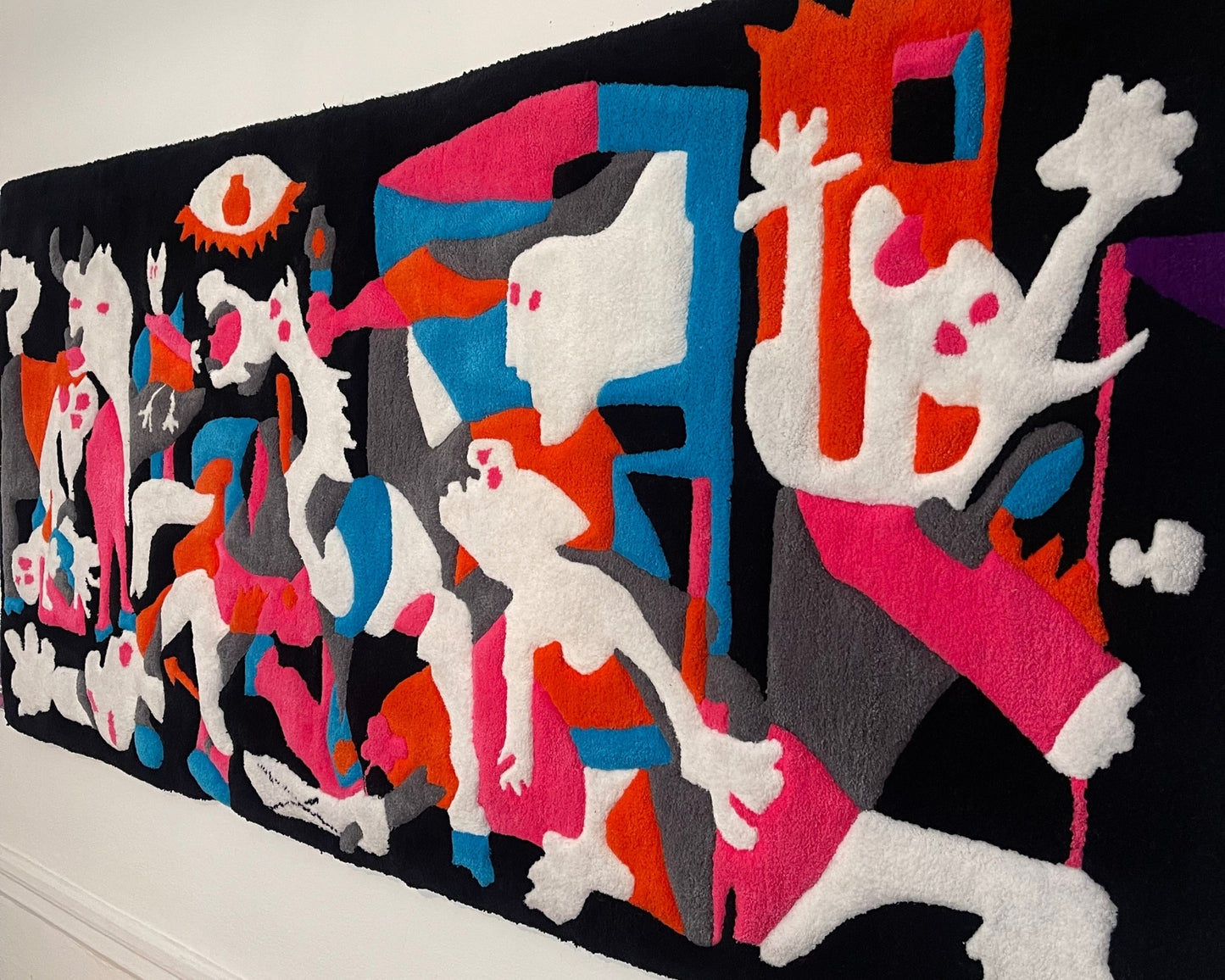 Zoom sur un tapis mural d’artiste. Détail saisissant de formes humaines stylisées, tissées à la main dans un contraste puissant de couleurs.